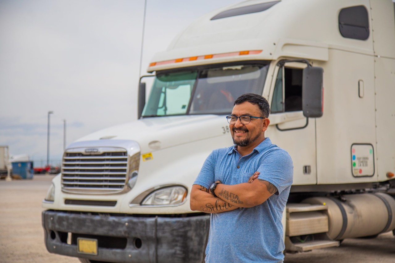 Tomas, and owner operator contracted with J.B. Hunt, stands in front of his truck and smiles.
