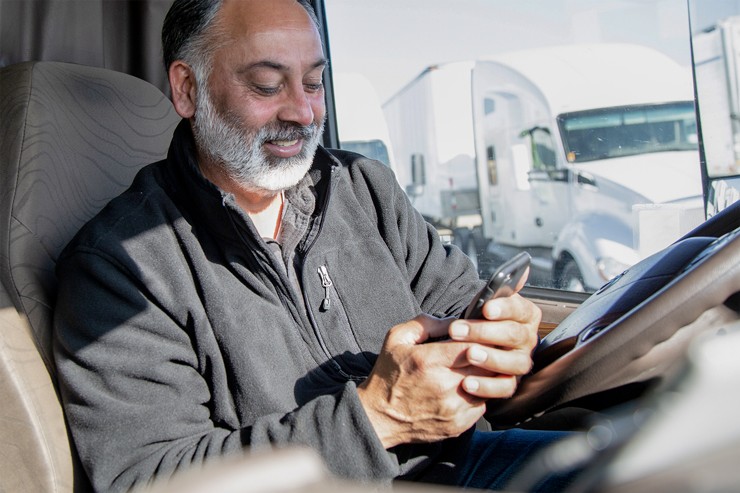 J.B. Hunt Driver on phone photo of a J.B. Hunt driver sitting in the cab of a truck smiling at his phone