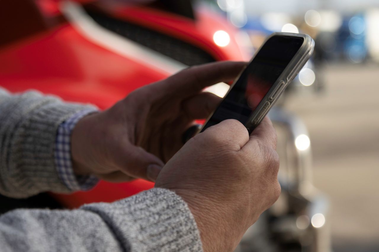 Close-up of a person holding and using a smartphone outdoors with a red semi‑truck visible in the background.